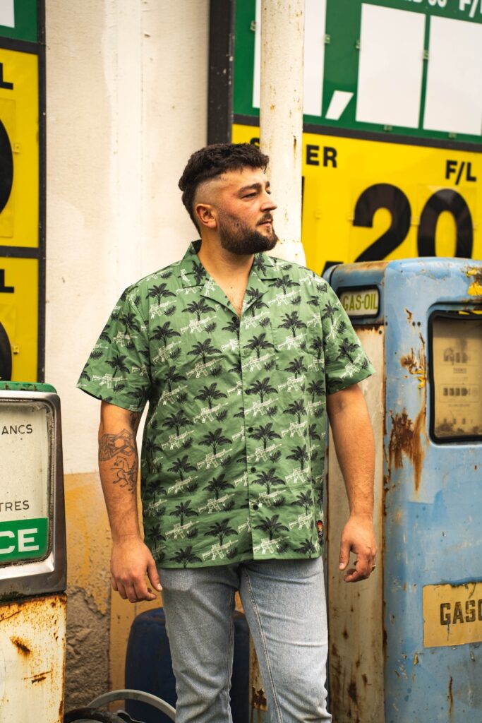 Homme portant une chemise verte style Western devant des pompes à essence vintage, ambiance outdoor rétro