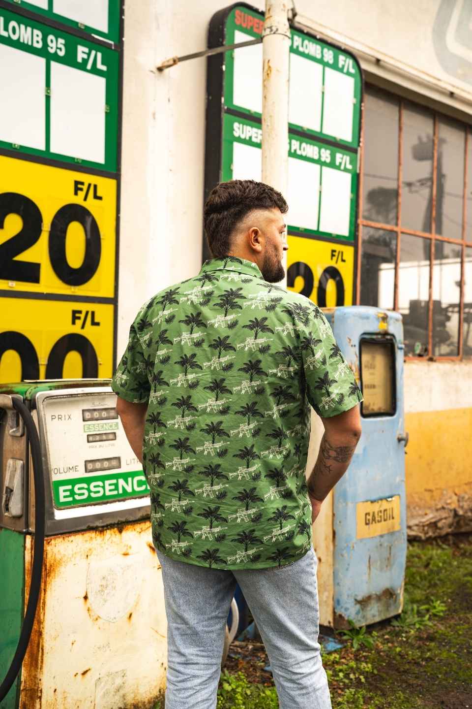 Dos d’un homme portant une chemise western verte style chasse et outdoor devant une station-service vintage